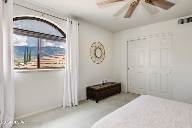 bedroom with light carpet, a closet, a mountain view, and ceiling fan