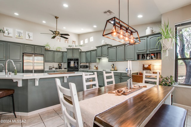 kitchen featuring tasteful backsplash, appliances with stainless steel finishes, ceiling fan with notable chandelier, green cabinets, and light tile patterned floors