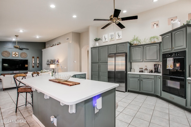 kitchen featuring sink, double oven, stainless steel refrigerator, light tile patterned floors, and a kitchen island with sink