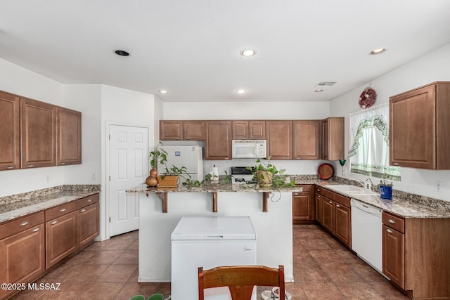 kitchen featuring light stone counters, a sink, a breakfast bar, white appliances, and visible vents