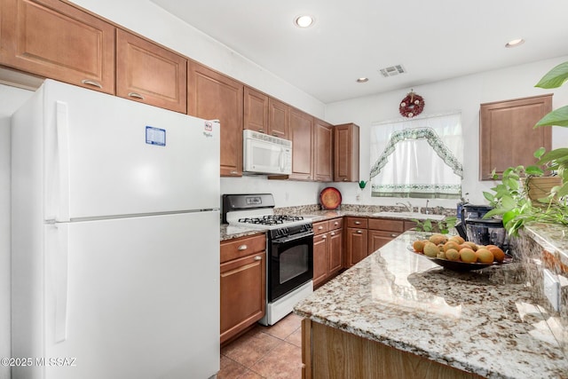 kitchen featuring visible vents, brown cabinetry, light stone counters, and white appliances