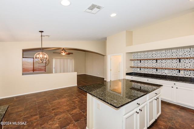 kitchen with ceiling fan with notable chandelier, dark stone countertops, white cabinetry, and hanging light fixtures