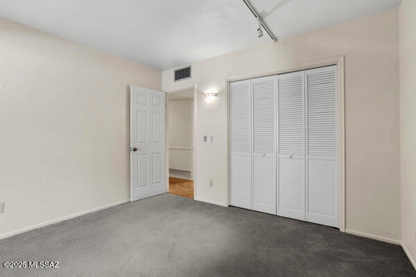 unfurnished bedroom featuring rail lighting, dark carpet, and a closet