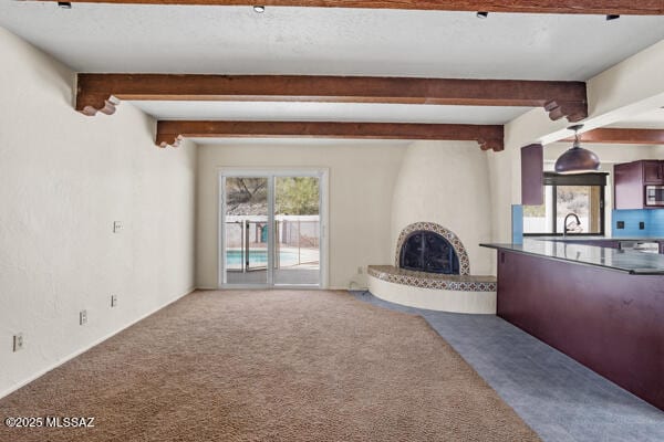 unfurnished living room featuring sink, a fireplace, beam ceiling, and carpet