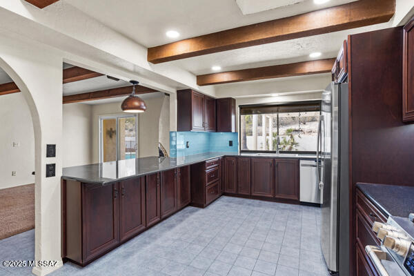 kitchen with decorative light fixtures, appliances with stainless steel finishes, kitchen peninsula, beamed ceiling, and backsplash