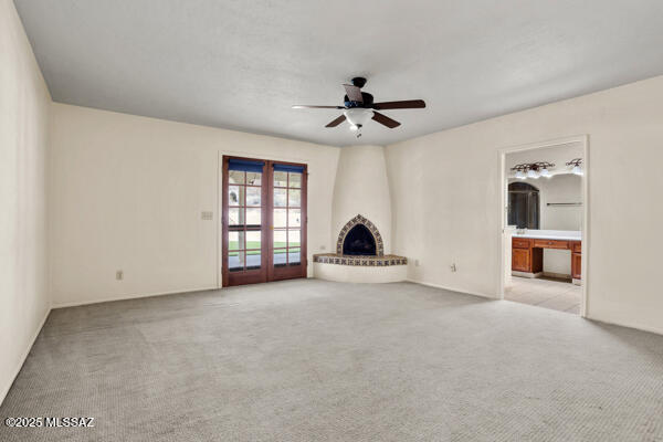 unfurnished living room with ceiling fan, light colored carpet, a fireplace, and french doors