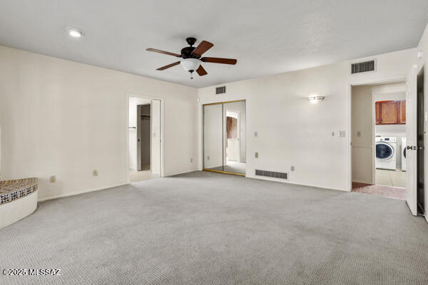 unfurnished living room featuring washer / dryer, light carpet, and ceiling fan