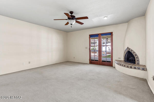 unfurnished living room featuring a brick fireplace, light colored carpet, french doors, and ceiling fan