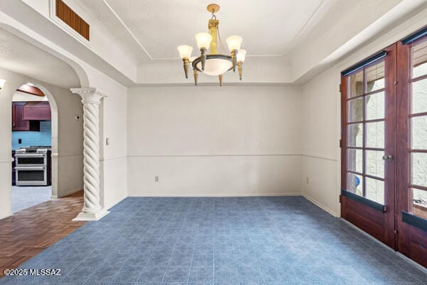 unfurnished room featuring an inviting chandelier, decorative columns, and french doors