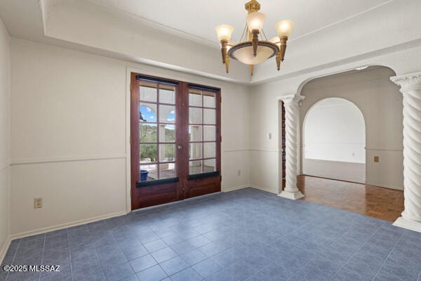 unfurnished room featuring french doors, an inviting chandelier, a tray ceiling, and decorative columns