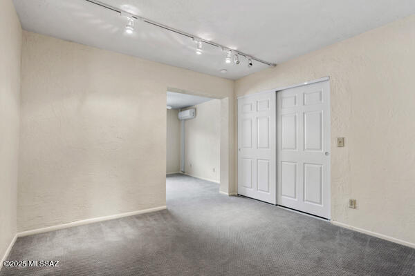 empty room with track lighting, a wall unit AC, and carpet flooring