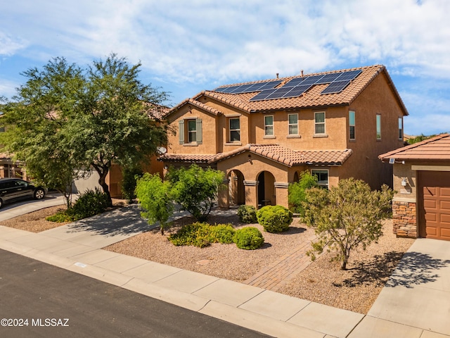 mediterranean / spanish home with concrete driveway, stone siding, a tiled roof, roof mounted solar panels, and stucco siding