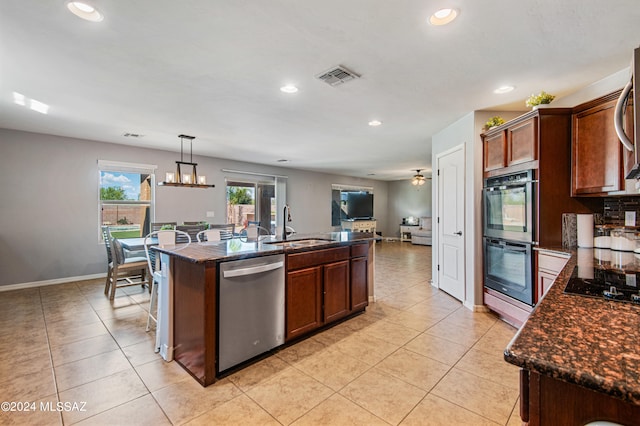 kitchen with pendant lighting, an island with sink, light tile patterned floors, sink, and black appliances