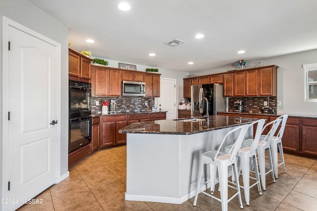 kitchen with a kitchen island with sink, appliances with stainless steel finishes, light tile patterned flooring, and decorative backsplash