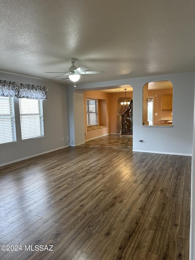 unfurnished living room featuring ceiling fan with notable chandelier, dark hardwood / wood-style flooring, and a textured ceiling