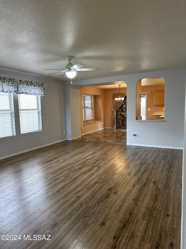 unfurnished living room featuring dark wood-type flooring, ceiling fan with notable chandelier, and a textured ceiling