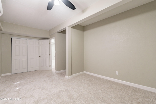 unfurnished bedroom with ceiling fan, a wall mounted air conditioner, light colored carpet, and a closet