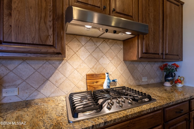 kitchen featuring dark brown cabinetry, tasteful backsplash, stainless steel gas cooktop, and dark stone counters