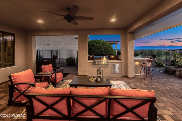 patio terrace at dusk featuring exterior bar, an outdoor living space, area for grilling, and ceiling fan