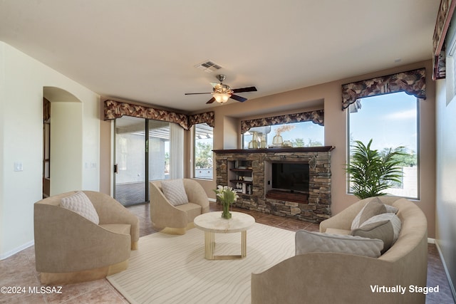 tiled living room with arched walkways, a fireplace, visible vents, a ceiling fan, and baseboards