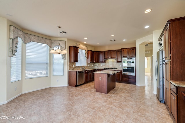 kitchen featuring tasteful backsplash, arched walkways, a kitchen island, appliances with stainless steel finishes, and a sink