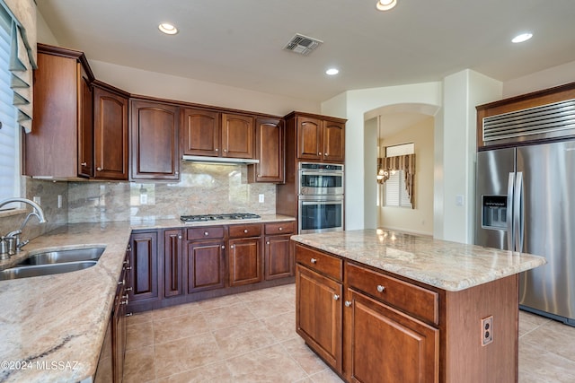 kitchen with arched walkways, stainless steel appliances, a sink, light stone countertops, and tasteful backsplash