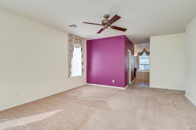 empty room with carpet floors, a wealth of natural light, visible vents, and baseboards