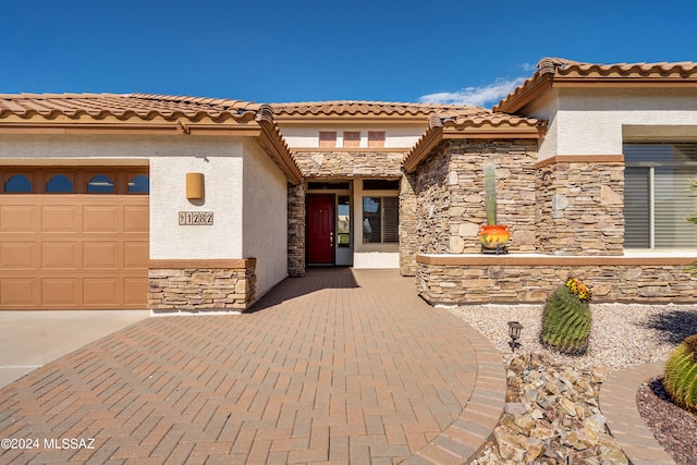 entrance to property with an attached garage, stone siding, and stucco siding