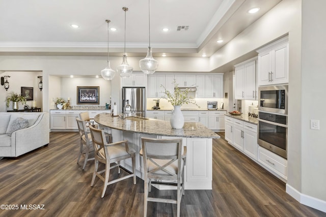 kitchen with a large island, sink, hanging light fixtures, stainless steel appliances, and white cabinets