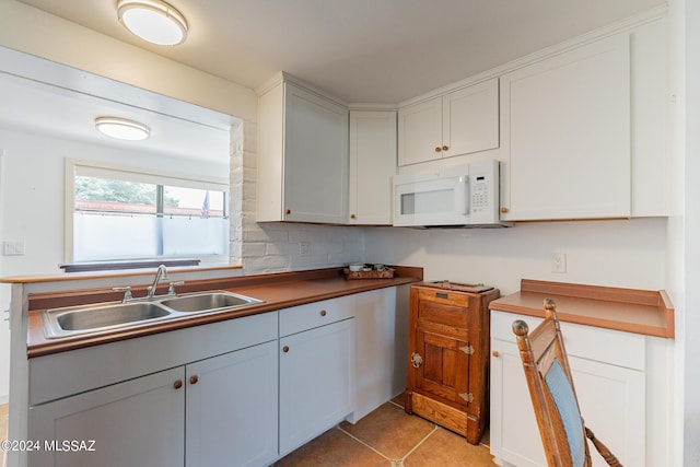 kitchen featuring white microwave, light tile patterned flooring, a sink, and white cabinets