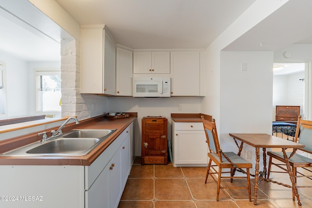 kitchen with white microwave, tile patterned flooring, white cabinets, and a sink