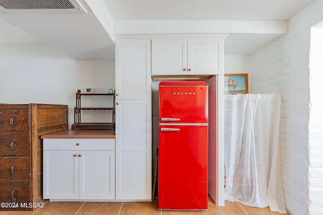 kitchen with light tile patterned floors, refrigerator, visible vents, white cabinetry, and dark countertops