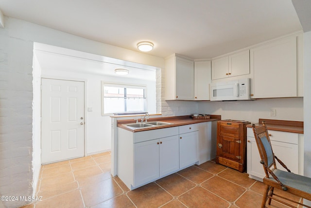 kitchen featuring white microwave, backsplash, a sink, and white cabinets