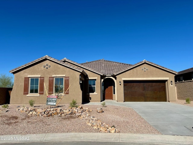 view of front facade with driveway, a tile roof, a garage, and stucco siding