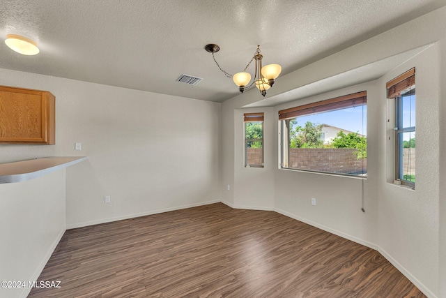 unfurnished dining area featuring a textured ceiling, an inviting chandelier, and dark hardwood / wood-style floors