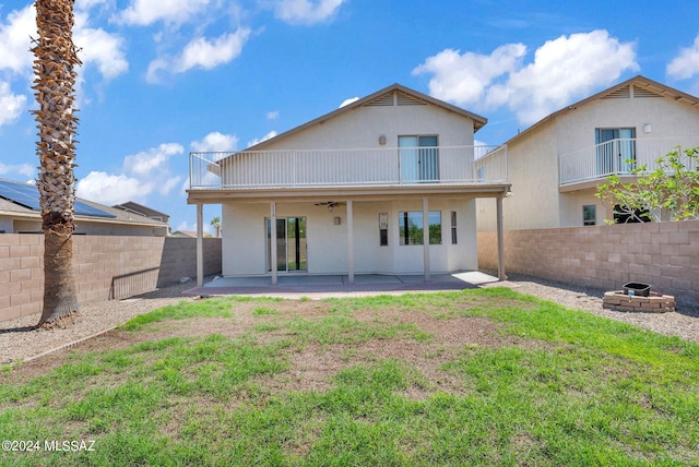 rear view of property featuring a patio, solar panels, a balcony, and a fire pit