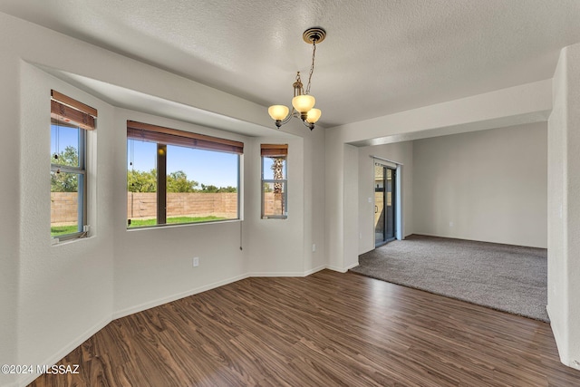 unfurnished room with a textured ceiling, an inviting chandelier, and dark hardwood / wood-style floors