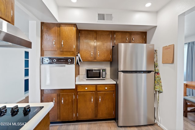 kitchen with appliances with stainless steel finishes, light hardwood / wood-style floors, and wall chimney range hood