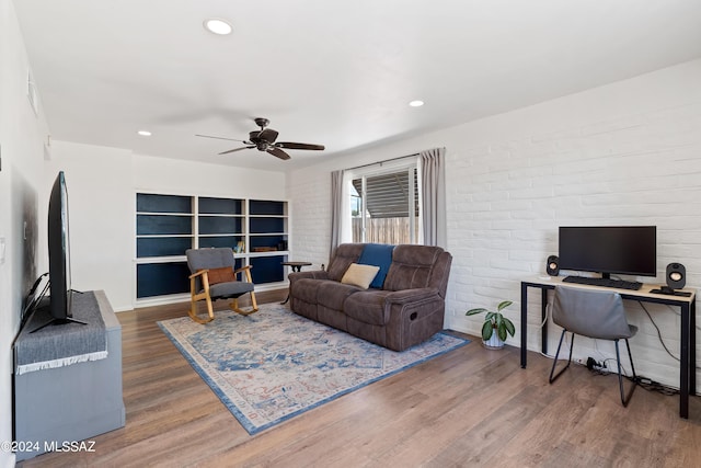 living room featuring dark hardwood / wood-style flooring, ceiling fan, and brick wall