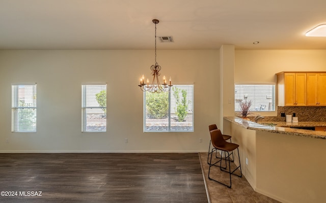 kitchen featuring decorative backsplash, a chandelier, light brown cabinetry, and dark wood-type flooring