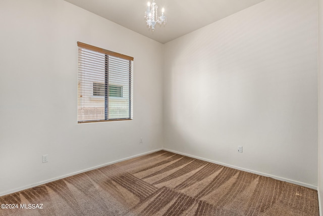 carpeted spare room featuring an inviting chandelier