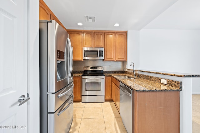 kitchen featuring light tile patterned flooring, sink, kitchen peninsula, stainless steel appliances, and dark stone countertops