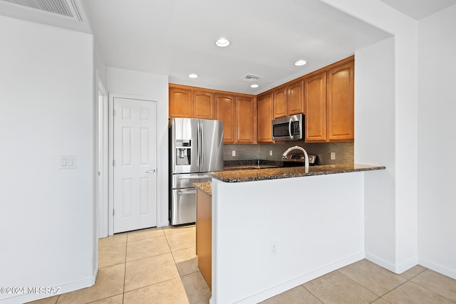 kitchen featuring light tile patterned flooring, kitchen peninsula, tasteful backsplash, appliances with stainless steel finishes, and dark stone countertops