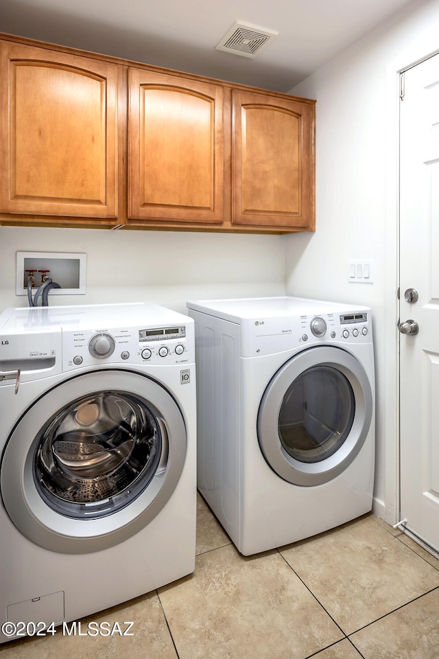 clothes washing area featuring cabinets, light tile patterned flooring, and washing machine and dryer