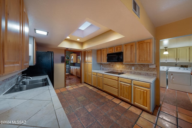 kitchen featuring tile counters, sink, black appliances, a skylight, and washer and clothes dryer