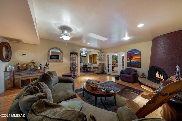 living room with light wood-type flooring, ceiling fan, a skylight, and a fireplace