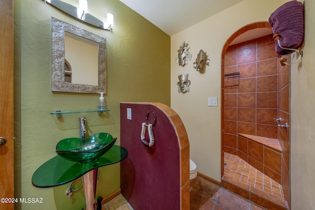 bathroom featuring a tile shower, sink, and toilet