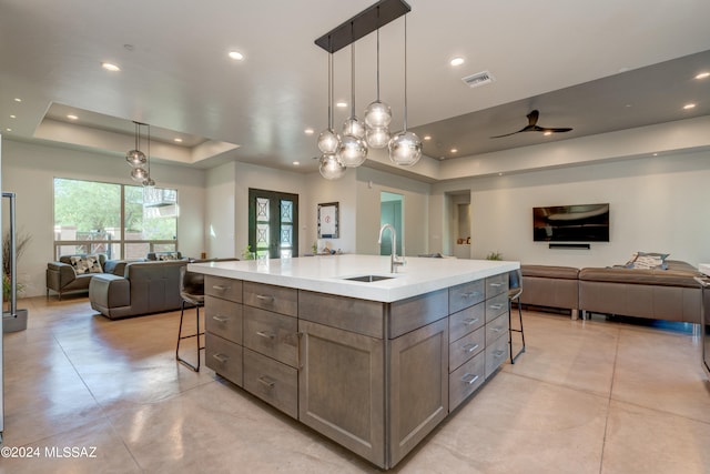 kitchen with a tray ceiling, ceiling fan, a kitchen island with sink, and a breakfast bar