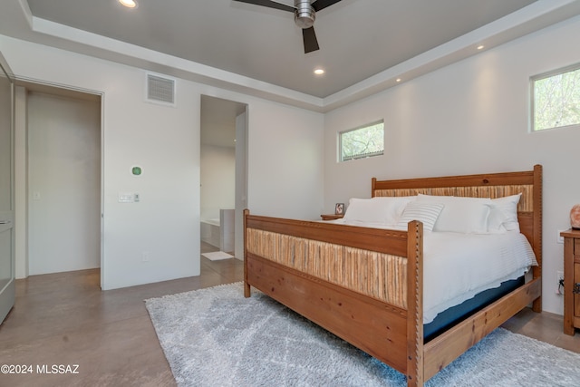 bedroom with ceiling fan, ensuite bath, and a tray ceiling