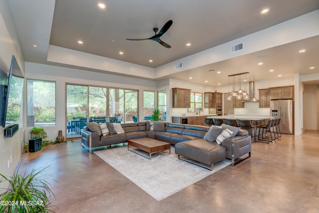 living room with ceiling fan with notable chandelier and a raised ceiling